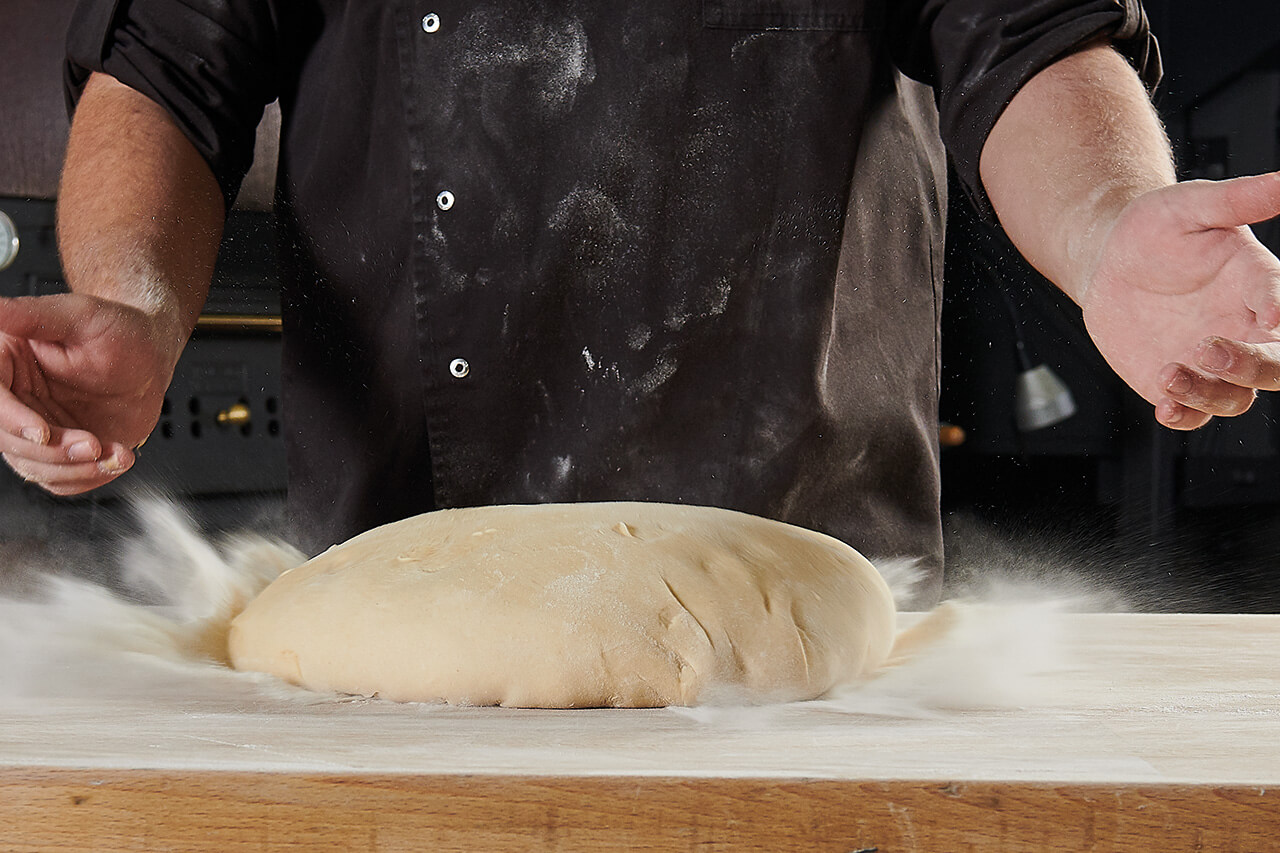 Perfekter Teig zum Weiterverarbeiten Bäcker wirft Teig auf Arbeitsfläche