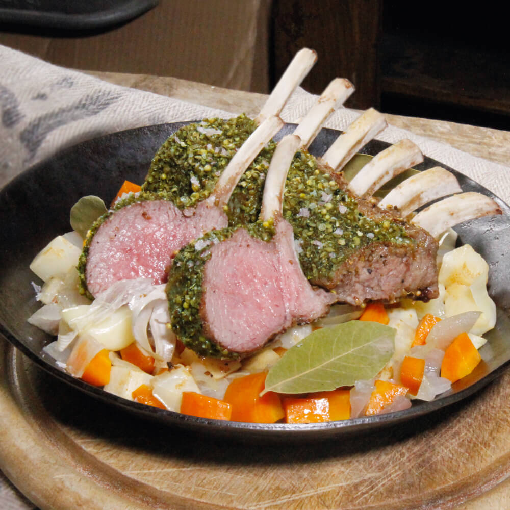 Rezept für Gebackenes Lammkarree mit Kräuterkruste rosa Gebackenes Lammkarree mit Kräutermantel auf gewürfeltem Sellerie und Karotten in einer Eisen-Bratpfanne serviert