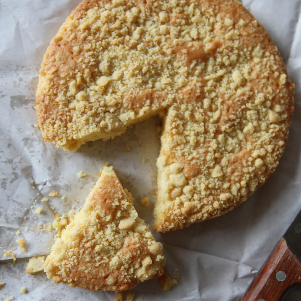 Rezept für Streuselkuchen Kuchen mit Streuseln oben drauf, bei dem ein Stück heraus geschnitten wurde auf einem weißen Tuch