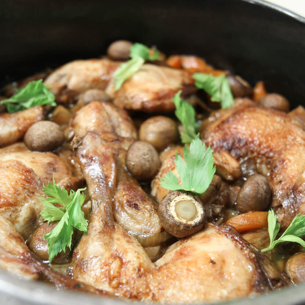 Rezept für Coq au vin Hähnchenschenkel mit Steinchampigions und frischer Petersilie in einem Schmortopf serviert
