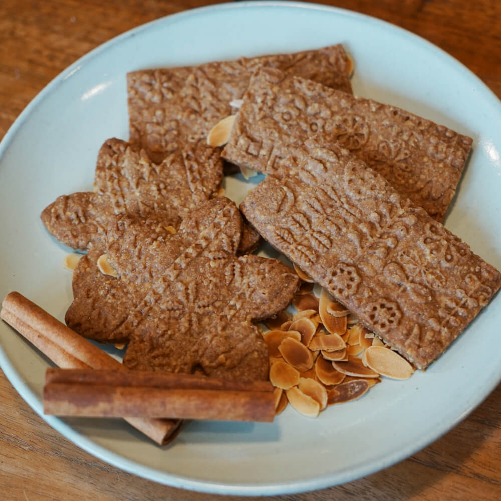 Rezept für Spekulatius selbstgemachter Spekulatius in Sternform mit Muster und in rechteckiger Form auf einem hellblauen Teller serviert mit ein paar gerösteten Mandelblättchen und Zimt