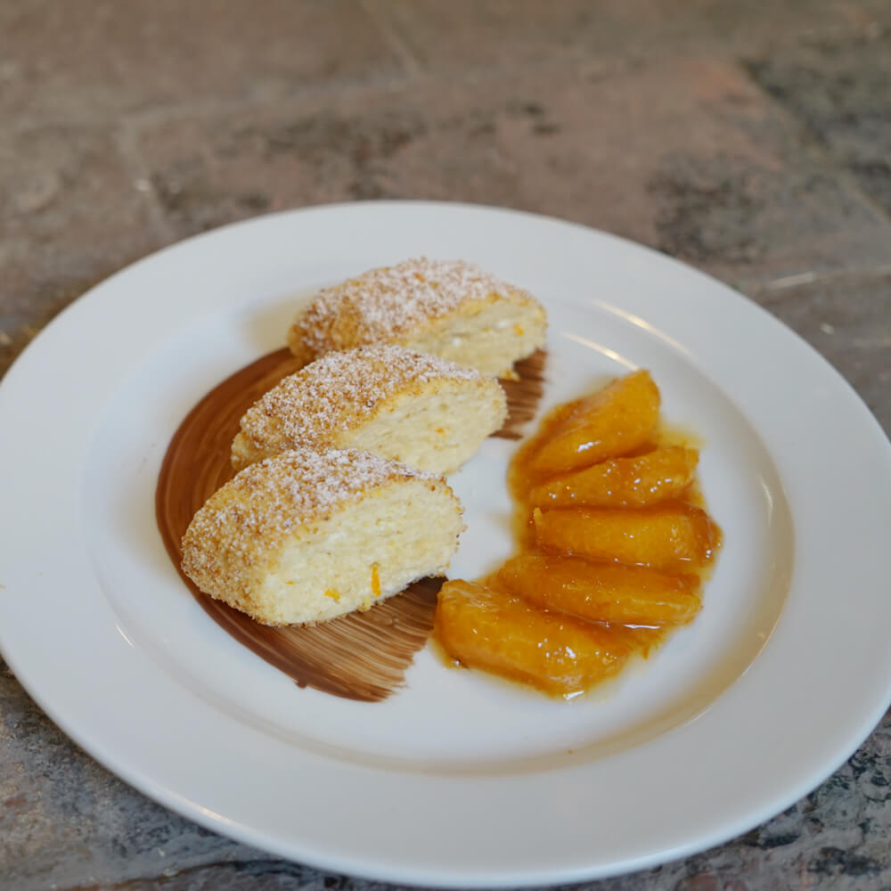 3 Stücke Topfenknödel mit Bröseln bestreut auf einem weißen Teller mit dem Orangenfilet-Kompott serviert