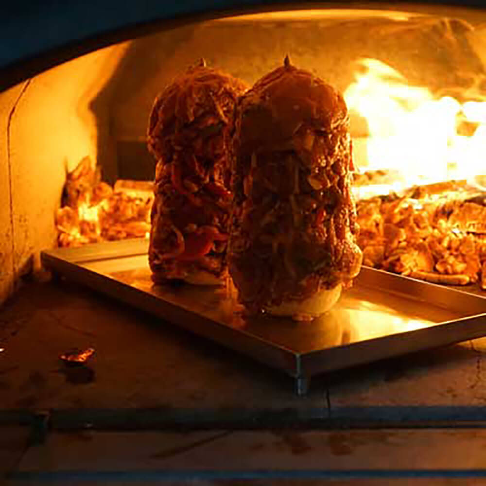 2 Gyrosspieße mit Fleisch und Gemüse geschichtet backen im Holzbackofen an der direkten Flamme und Glut
