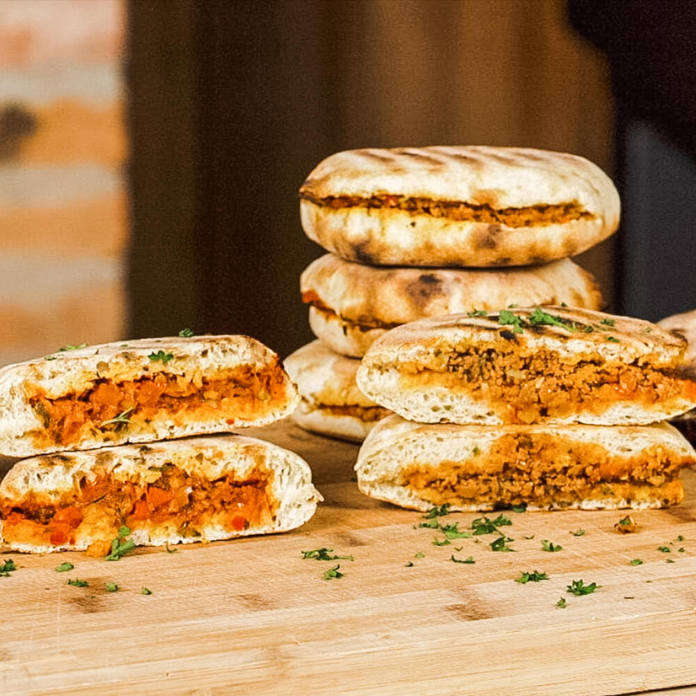 Rezept für Grilltaschen Zwei verschieden gefüllte Grilltaschen, eine mit Gemüse- und eine mit Fleischfüllung auf einem Holzbrett serviert und mit gehackter Petersilie dekoriert