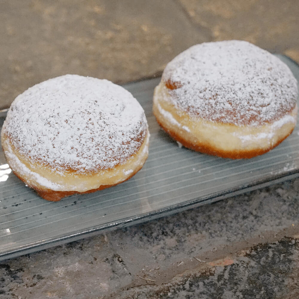 Rezept für Krapfen 2 Krapfen mit Puderzucker bestreut auf einer grauen länglichen Servierplatte