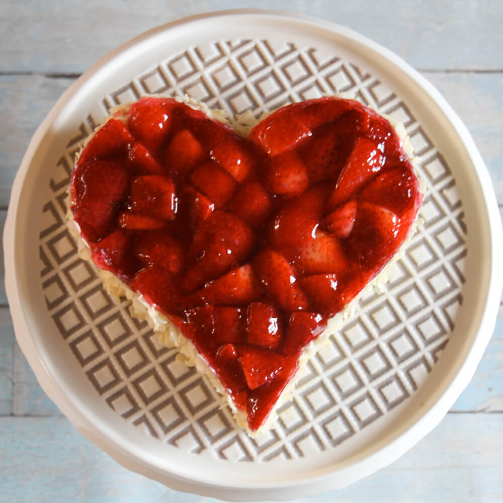 Herzförmiger Kuchen mit frischen Erdbeeren belegt - liebevoll dekoriertes Gebäck.