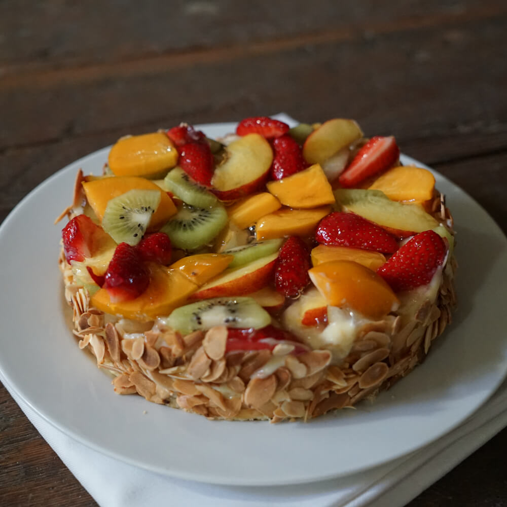 Obstkuchen mit frischem Obst wie Kiwi, Erdbeeren und Pfirsich. Gefüllt mit Vanillecreme und außen wurden gehobelte Mandeln angedrückt