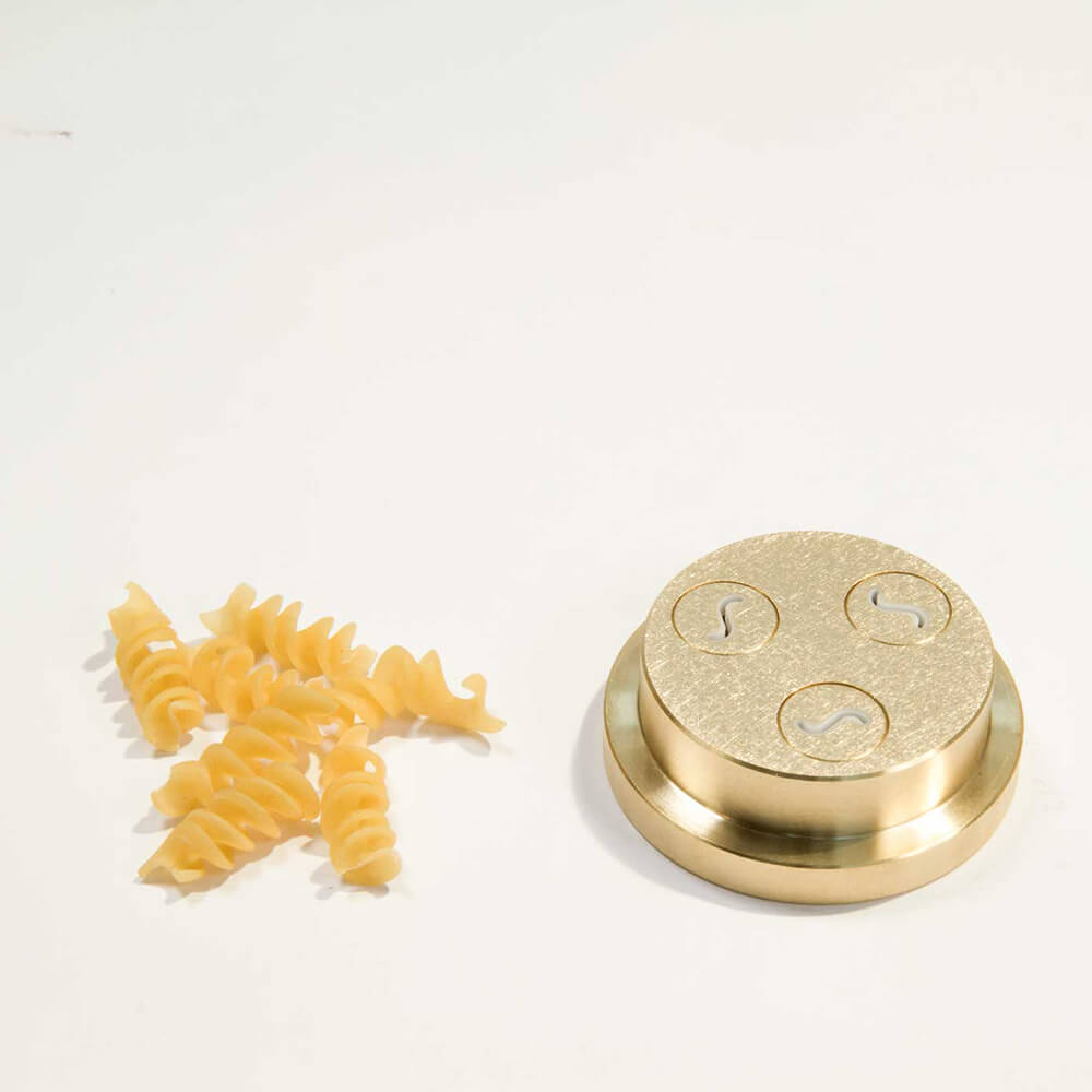 Matrize Nr. 49d - Fusilli/Spirelli Nudelmatrize Nr. 49d für Fusilli neben einigen Fusilli-Nudeln vor einem weißen Hintergrund.