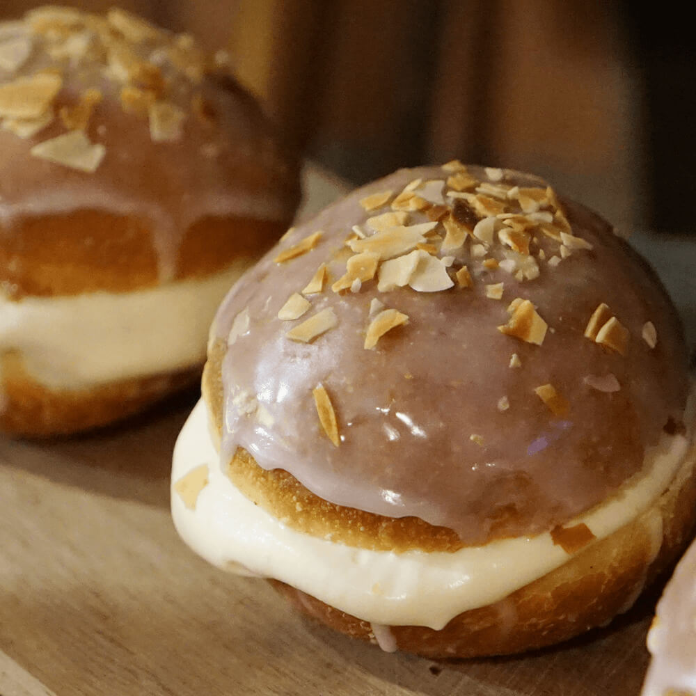 Rezept für Rezept für Krapfen mit Vanillefüllung 2 Krapfen mit einer Vanillefüllung, Zuckerguss oben drauf und ein paar Mandelblättchen auf einem Backbrett serviert