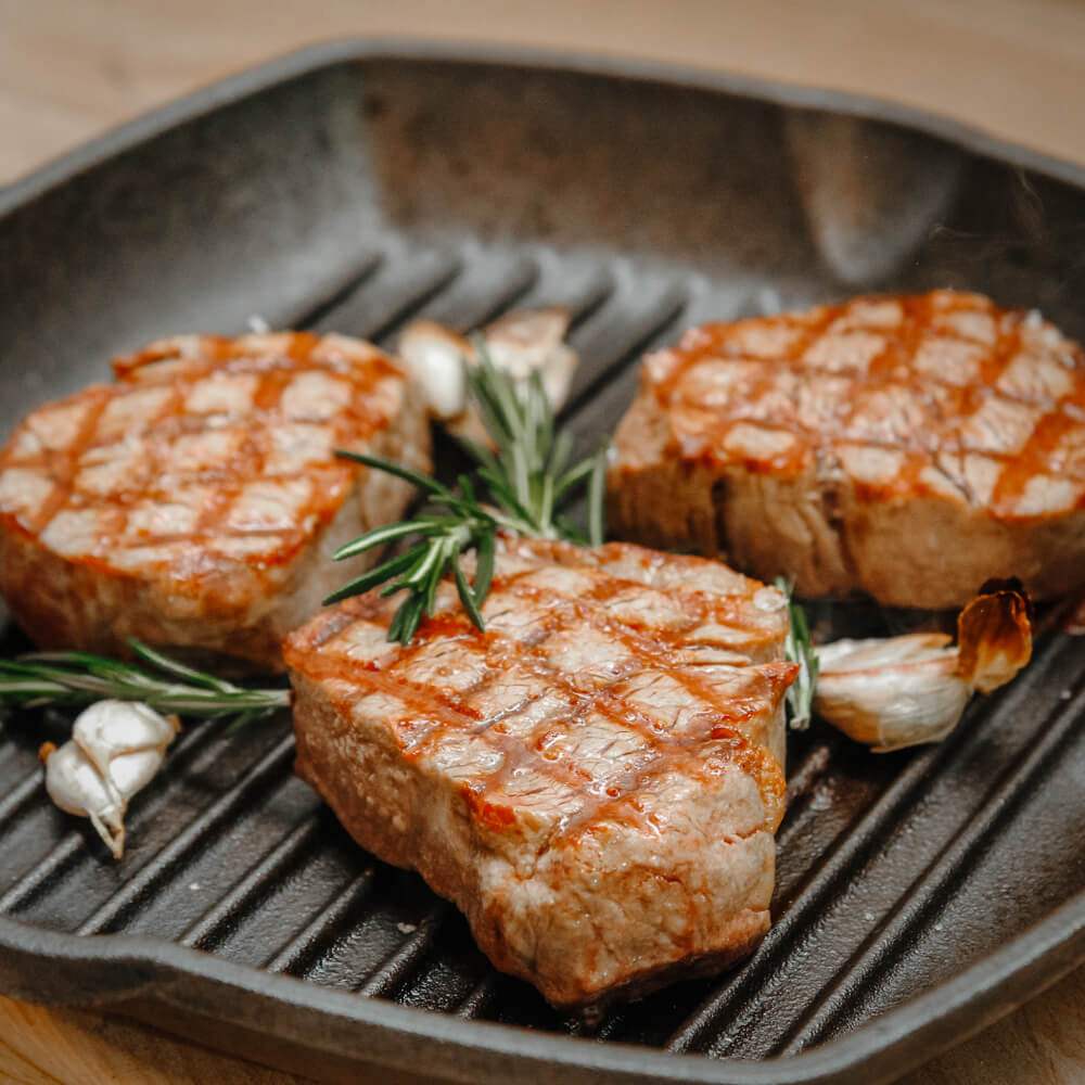 saftiges Rinderfiletsteak mit Rosmarinzweig und Knoblauchzehen in einer geriffelten Pfanne serviert