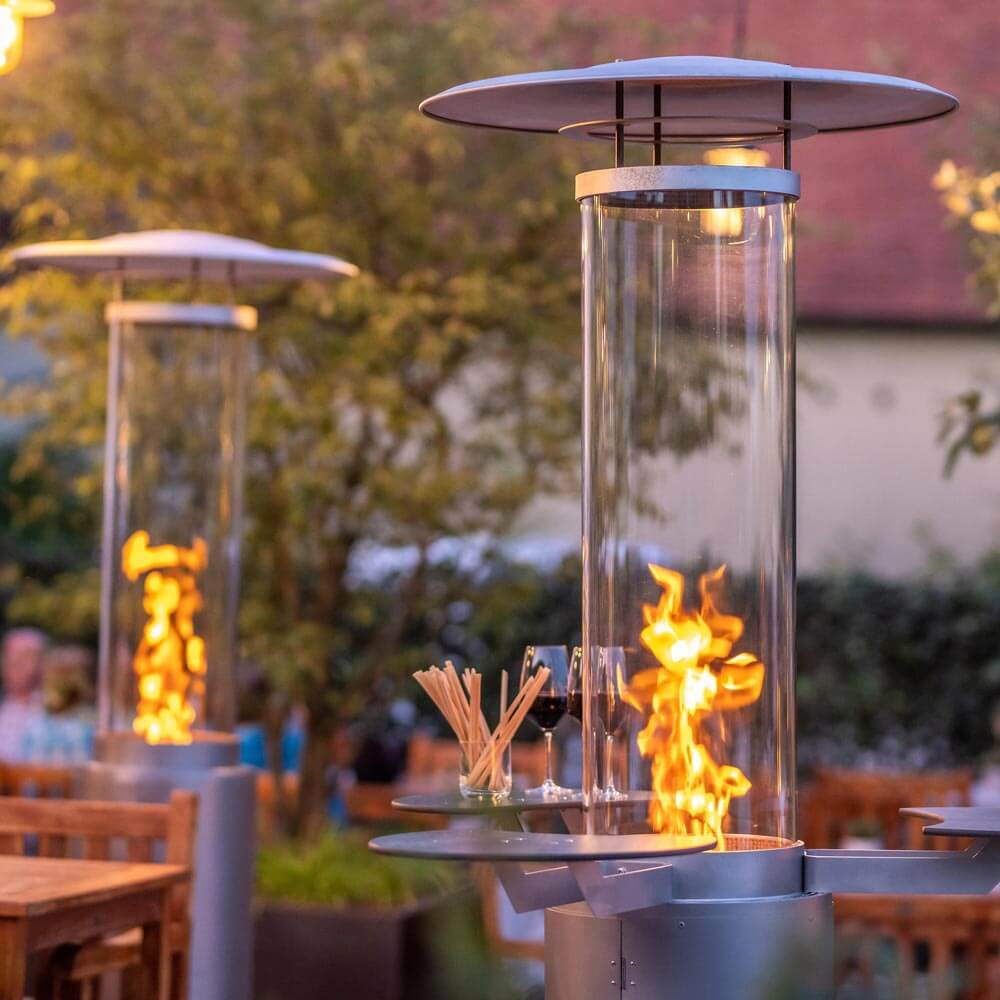 Zwei Terrassenstrahler mit angezündetem Feuer nebeneinander in einem Garten.