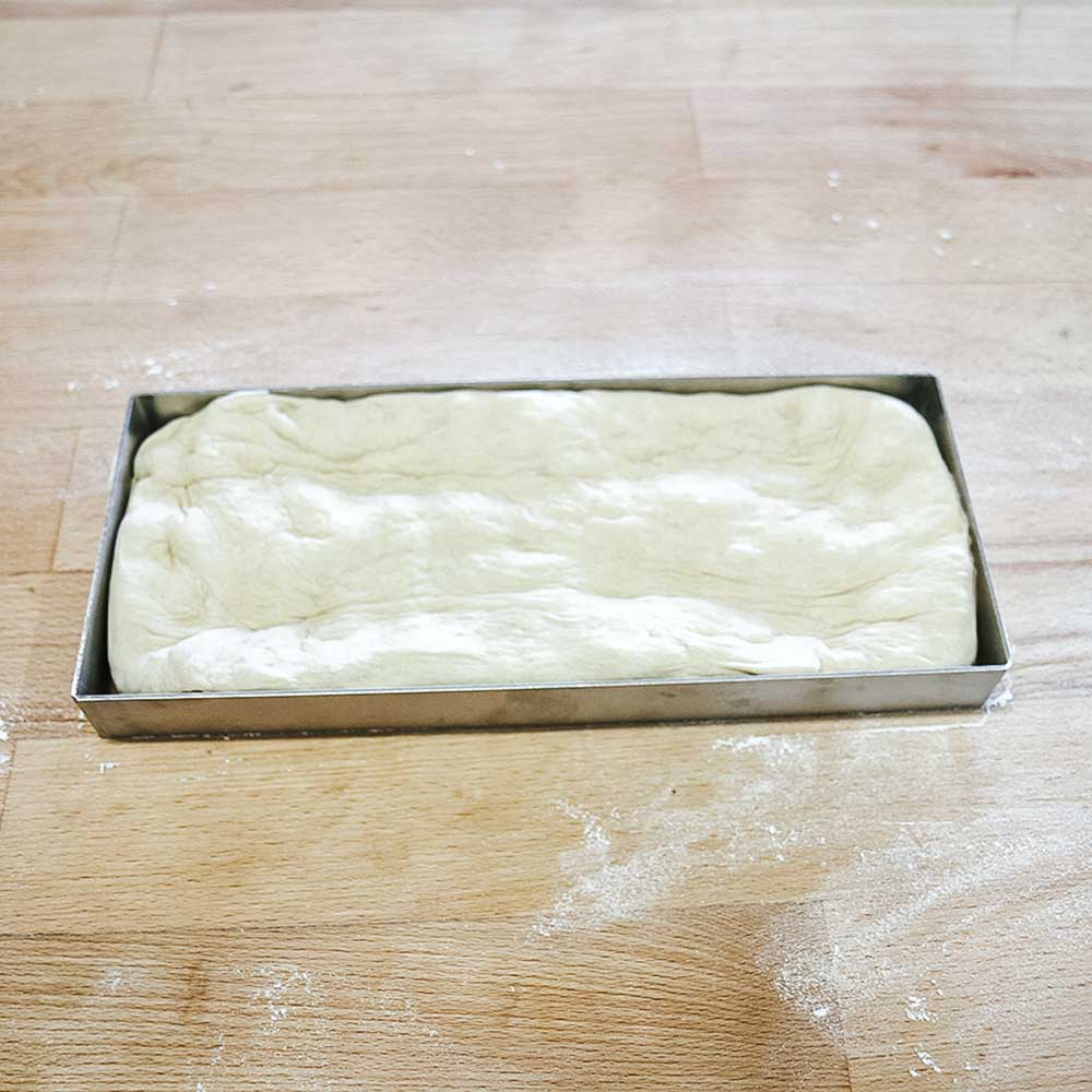 Teigteiler eckig Rahmen des Teigteilers mit Teig gefüllt auf einer Küchenarbeitsplatte.