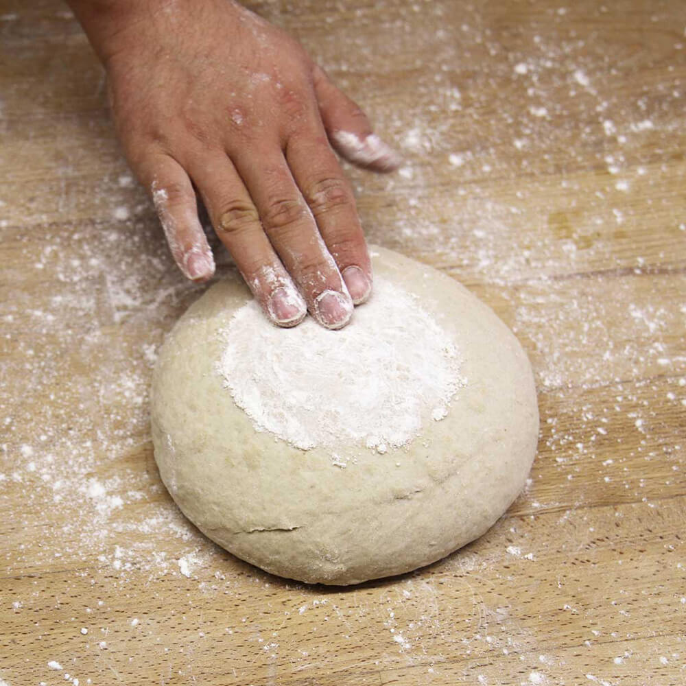 Brotstempel IHS rund geformter Brotteig mit Mehl bestäubt auf einem Holzbackbrett