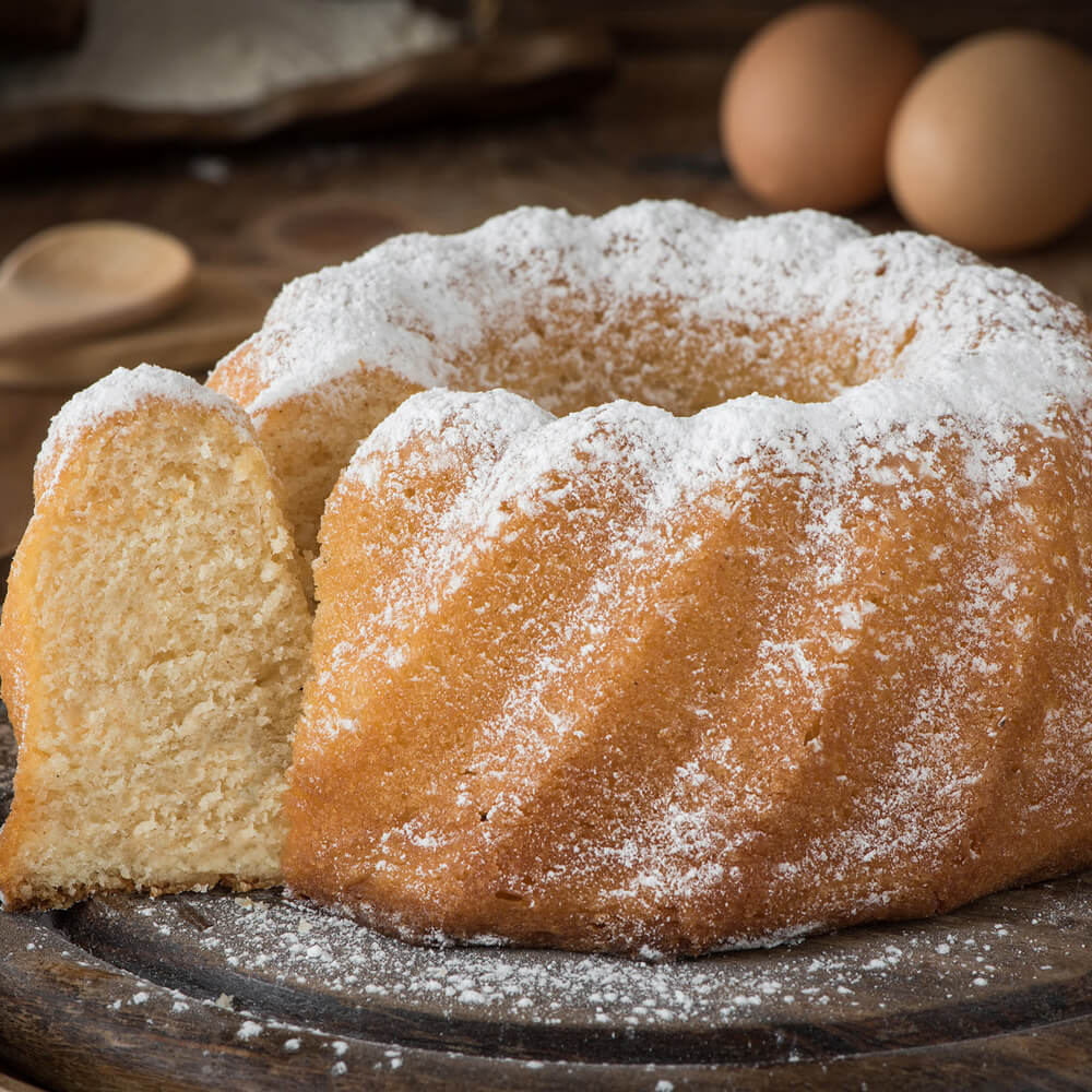 Rezept für Rührkuchen RÜhrkuchen in Gugelhupfform bestreut mit Puderzucker auf einer dunklen Kuchenplatte serviert