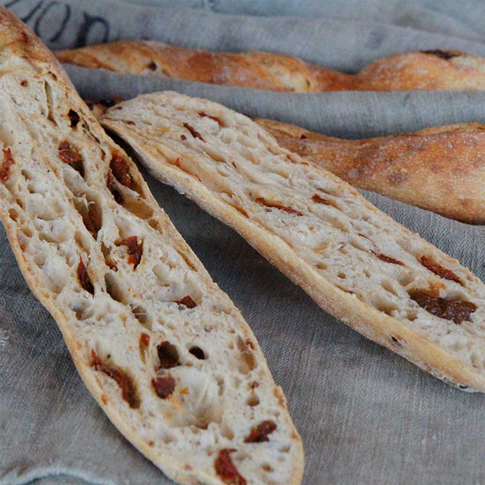 Französisches Baguettemehl Aufgeschnittenes Baguette mit Tomaten gefüllt auf einem Leinentuch liegend