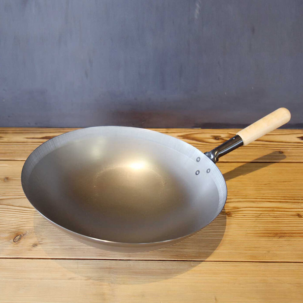 Wok aus Stahl mit praktischem Holzstiel auf einer Holzarbeitsplatte. 