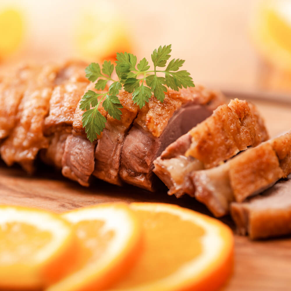 Rezept für Entenbrust saftige Entenbrust aufgeschnitten auf einem Holzbrett und mit frischen Kräutern und Orangenscheiben garniert