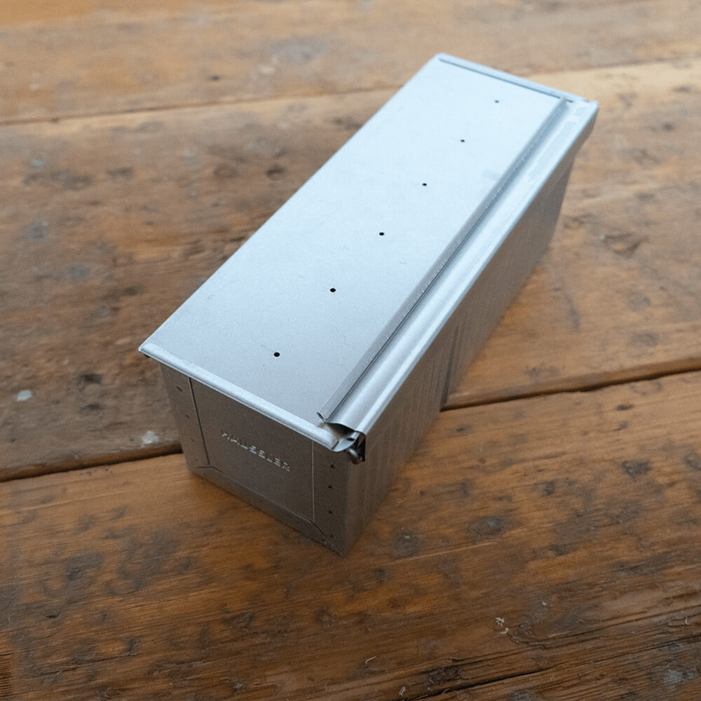 Große Toastbrotform Große Toastbrotform in seitlicher Ansicht aus aluminiertem Stahl auf einem Holz-Untergrund. Der Deckel ist geschlossen.