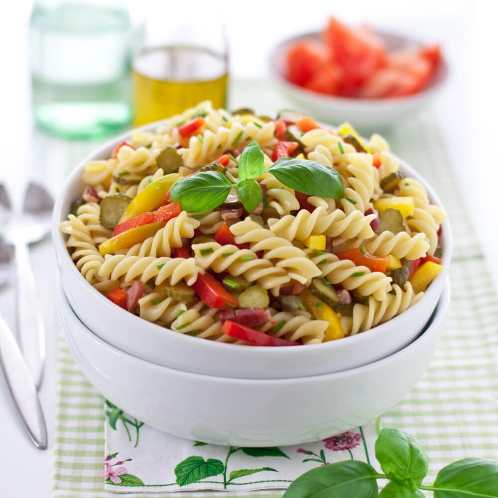Nudelsalat mit Spirelli, roter, gelber und grüner Parpika in einer weißen Schüssel serviert.