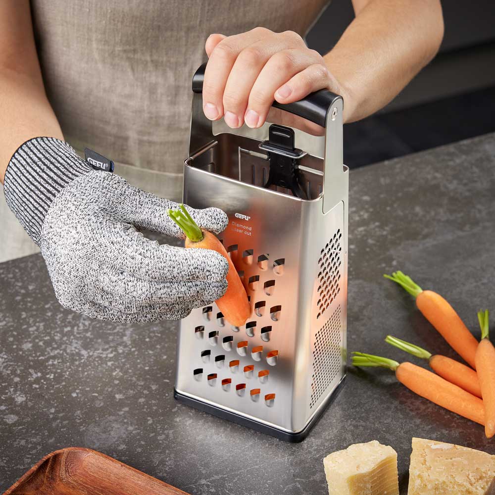 Schnittschutzhandschuh Eine Person hobelt eine Karotte auf einer Küchenarbeitslatte und trägt dabei den Schnittschutzhandschuh.