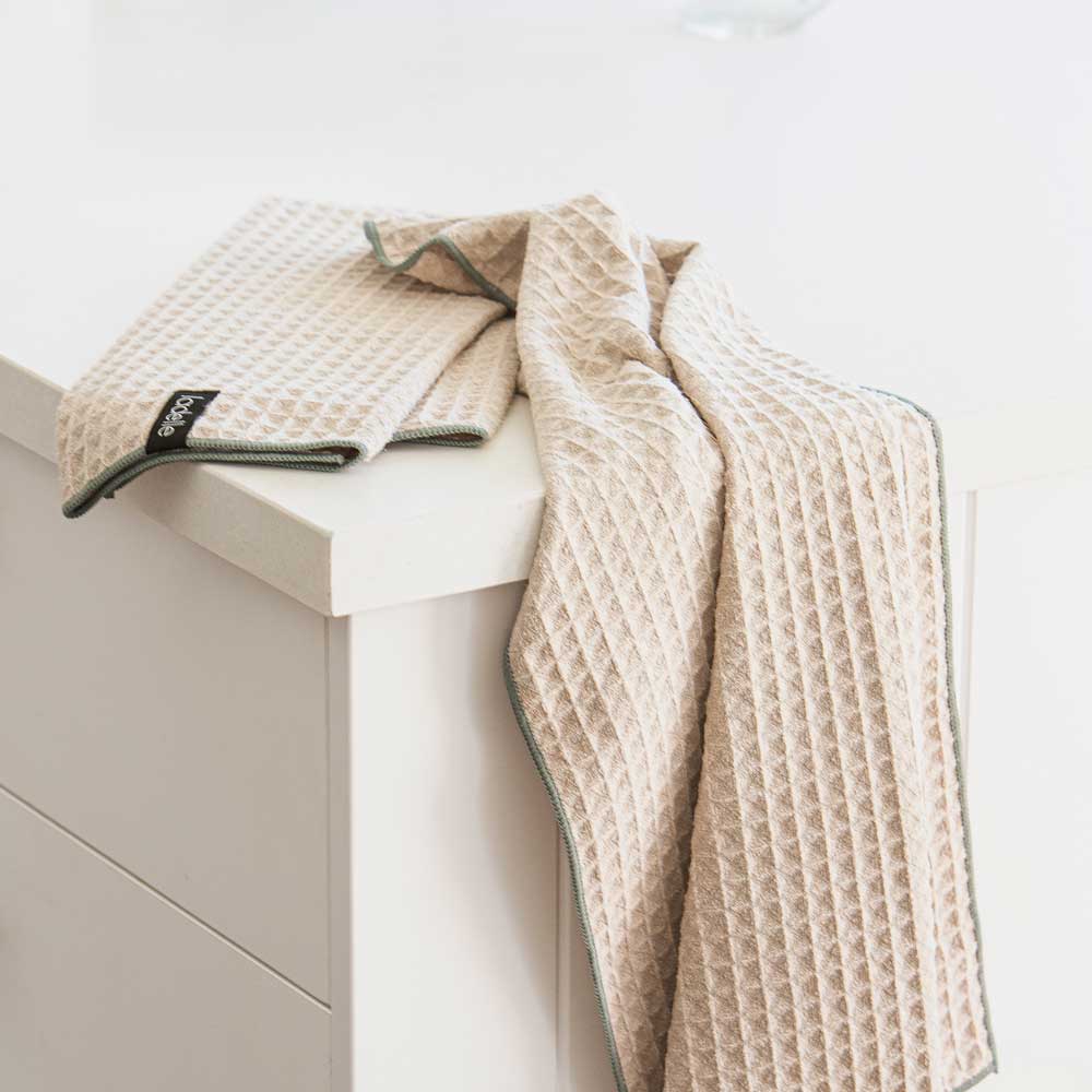 Geschirrtuch Mega Waffle auf einer Kommode neben einem gefalteten Geschirrtuch.