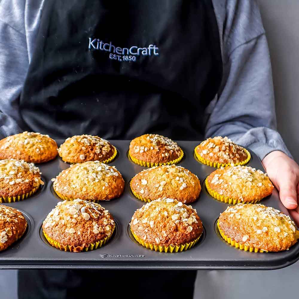 Muffinform mit 12 Mulden frische Muffins in Muffinbackform. Blech wird vom Bäcker gehalten