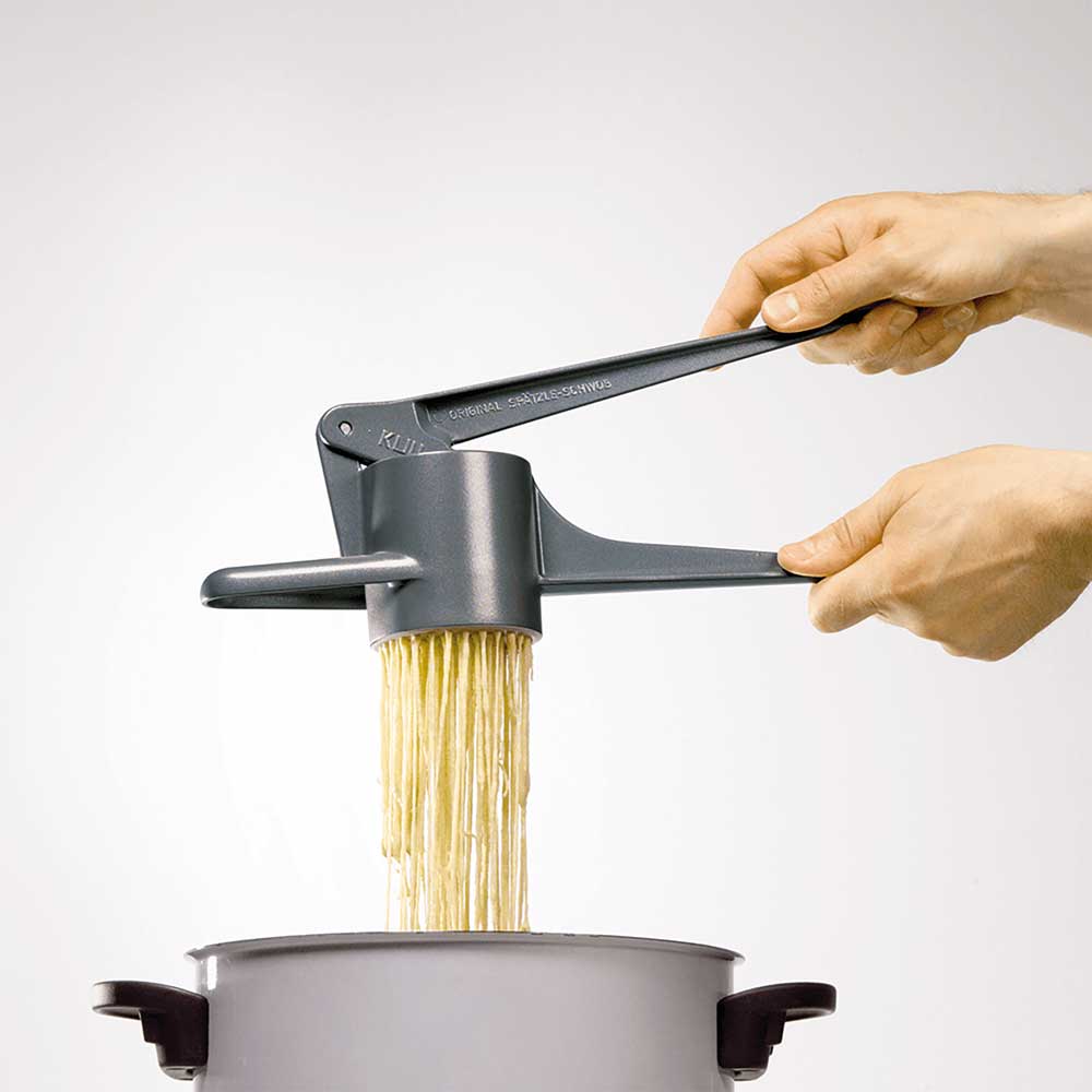 Spätzlepresse - Spätzle wie handgeschabt Zu sehen ist ein Topf und zwei Hände, die eine Spätzlepresse halten. Die gedrückten Spätzle fallen in den Topf.