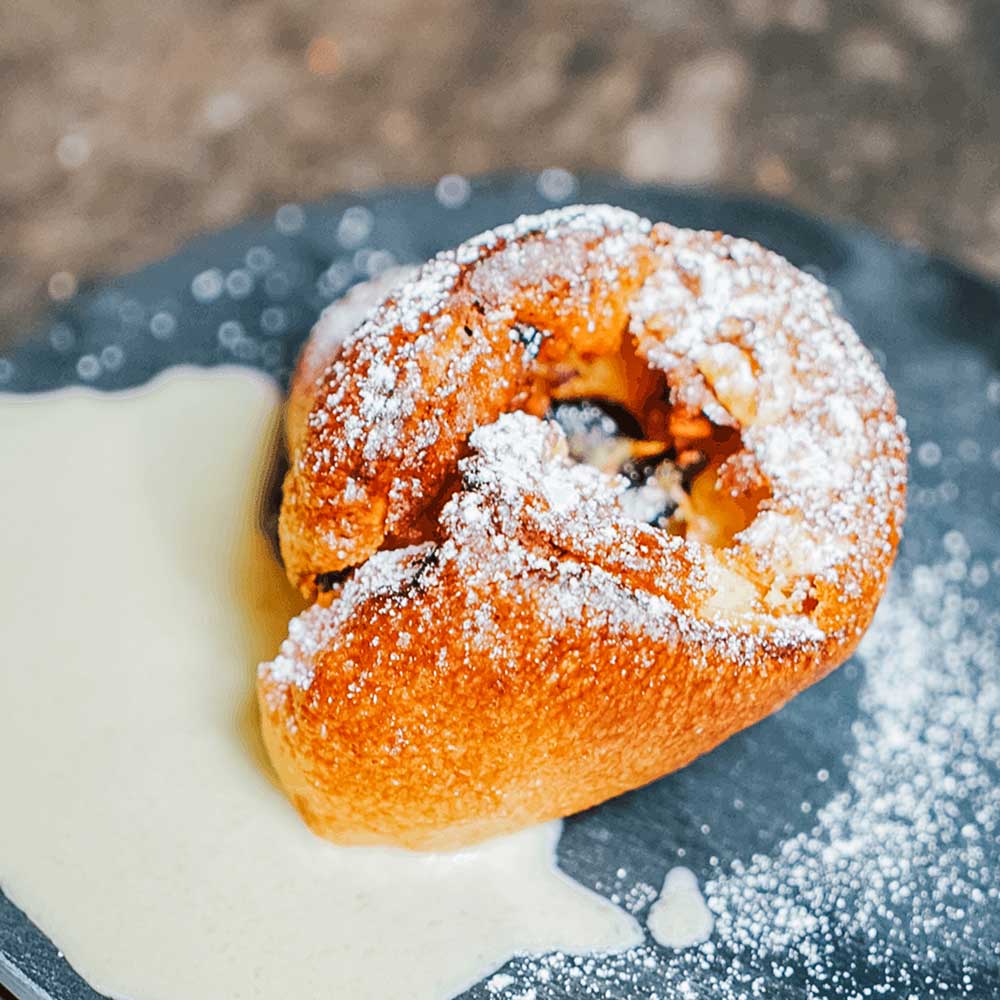 Pfitzaufgebäck mit Puderzucker bestreut. Das Gebäck liegt auf einer grauen Steinplatte
