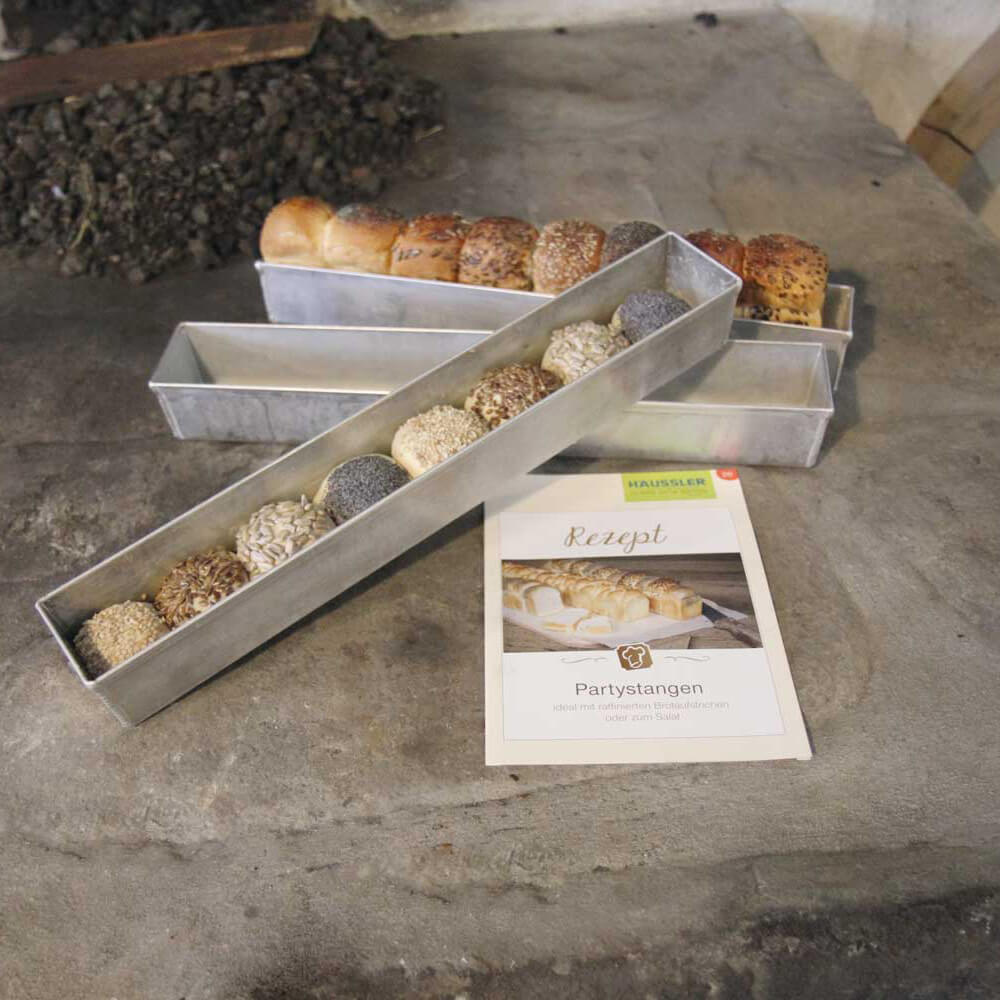 Drei verschiedene Partystangenformen auf einer Holzarbeitsplatte. In zwei der Formen sind Teiglinge mit verschiedenen Saaten als Partystange aufgereiht.