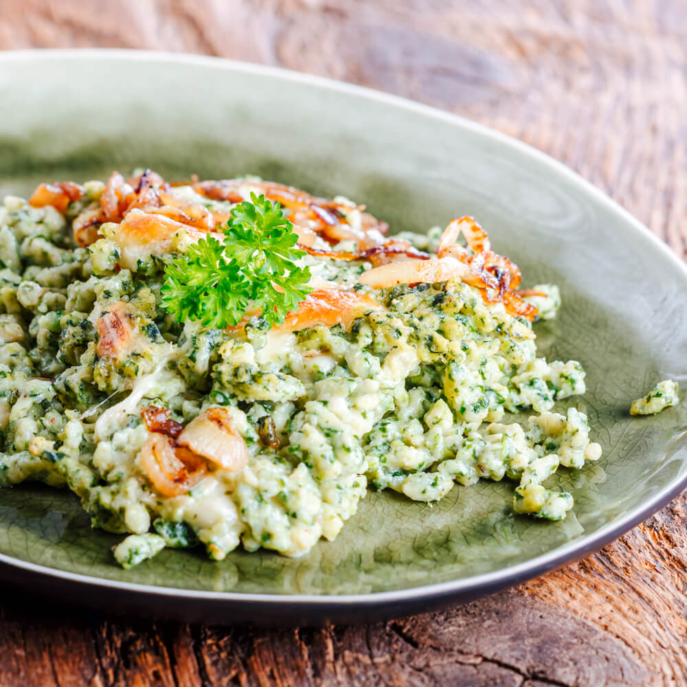 Rezept für Bärlauchspätzle grüne Bärlauchspätzle mit geschmelzten Zwiebeln auf einem grünen Teller serviert
