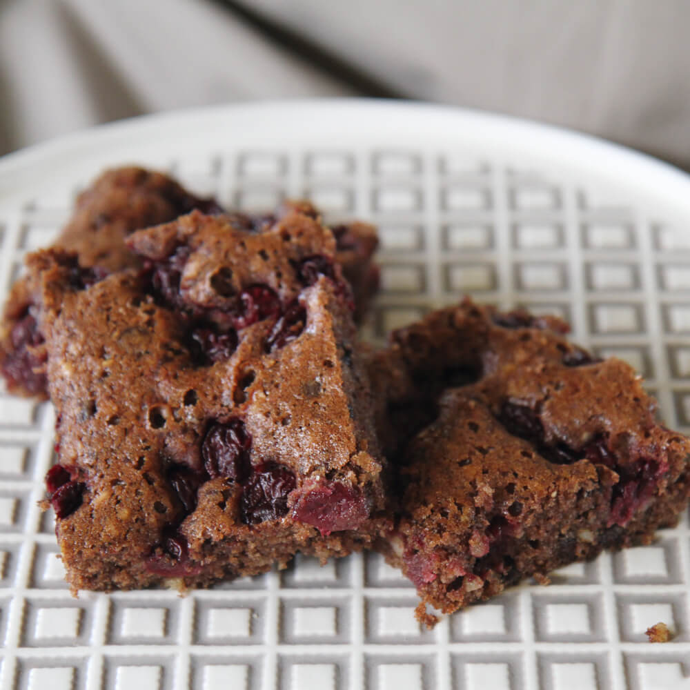 Rezept für Nussiger Schoko-Kirschkuchen 3 quadratische Stücke Nuss-Schoko-Kirschkuchen auf einer weiß-grau karierten Kuchenplatte serviert