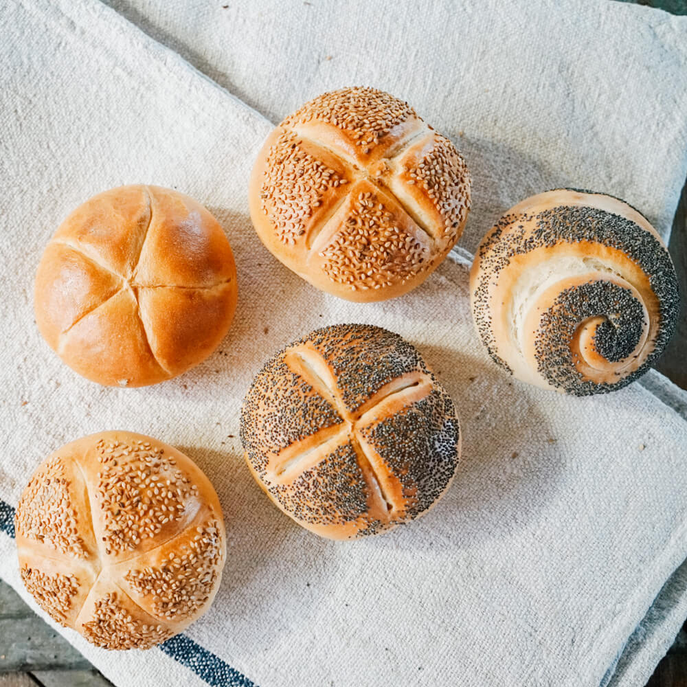 verschiedene Brötchen mit Sesam und Mohn auf einem grauen Tuch