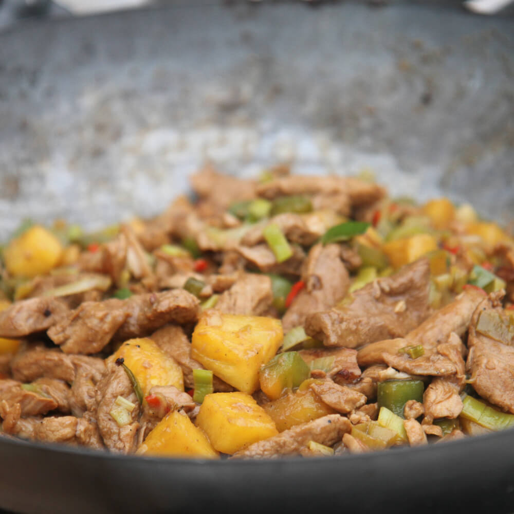 Rezept für Schweinefileltpfanne sueß-sauer mit feinen Nudeln Schweinefilet in Streifen geschnitten, zusammen mit Ananas, grüner Paprika, roter Chilli in einem Wok serviert