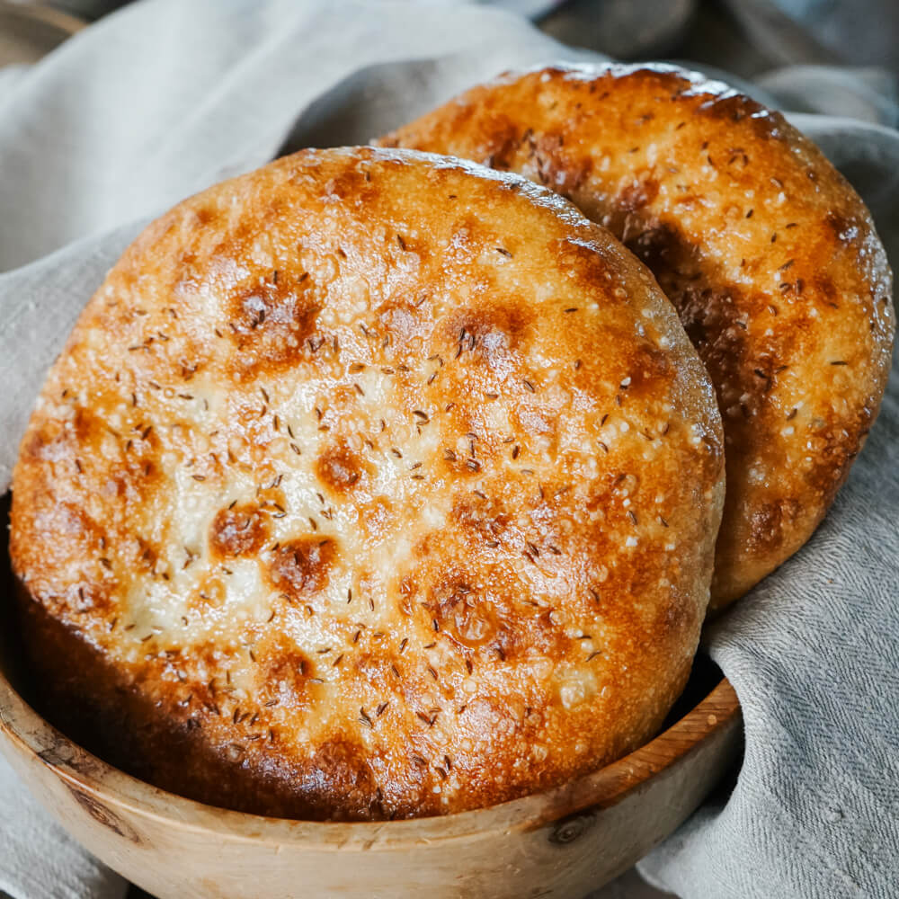 Salz-Kümmel Dinnete mit Langzeitführung frisch gebackene Dinnete mit Salz und Kümmel bestreut in einem Brotkorb aus Holz und mit einem grauen Geschirrtuch