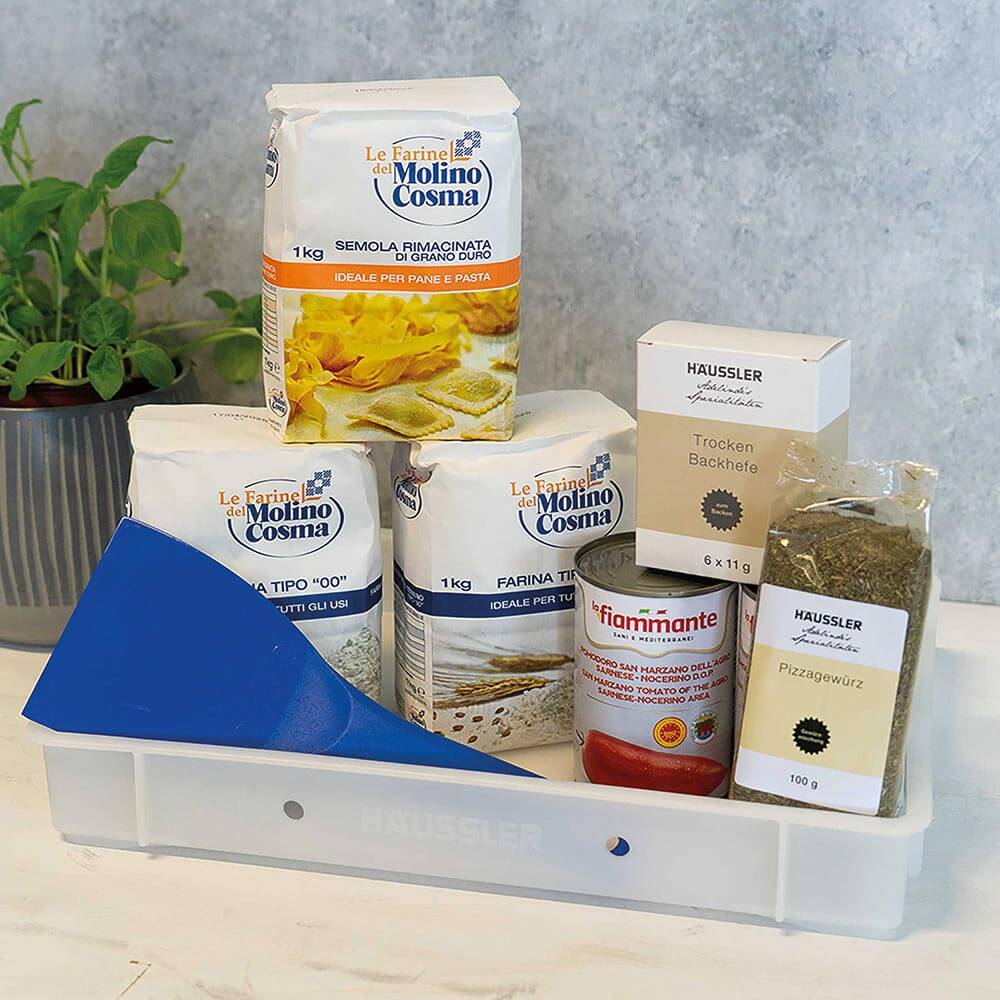 Auf dem Bild befindet sich eine weiße Gärbox mit vier Teiglingen. Zudem 2 verschiedene Mehle mit jeweils 1 Kilogramm Inhalt, eine Verpackung mit Trockenbackhefe 6 x 11 Gramm, 2 Dosen mit 400 Gramm geschälten Tomaten und ein blauer Plastik Teigschaber.