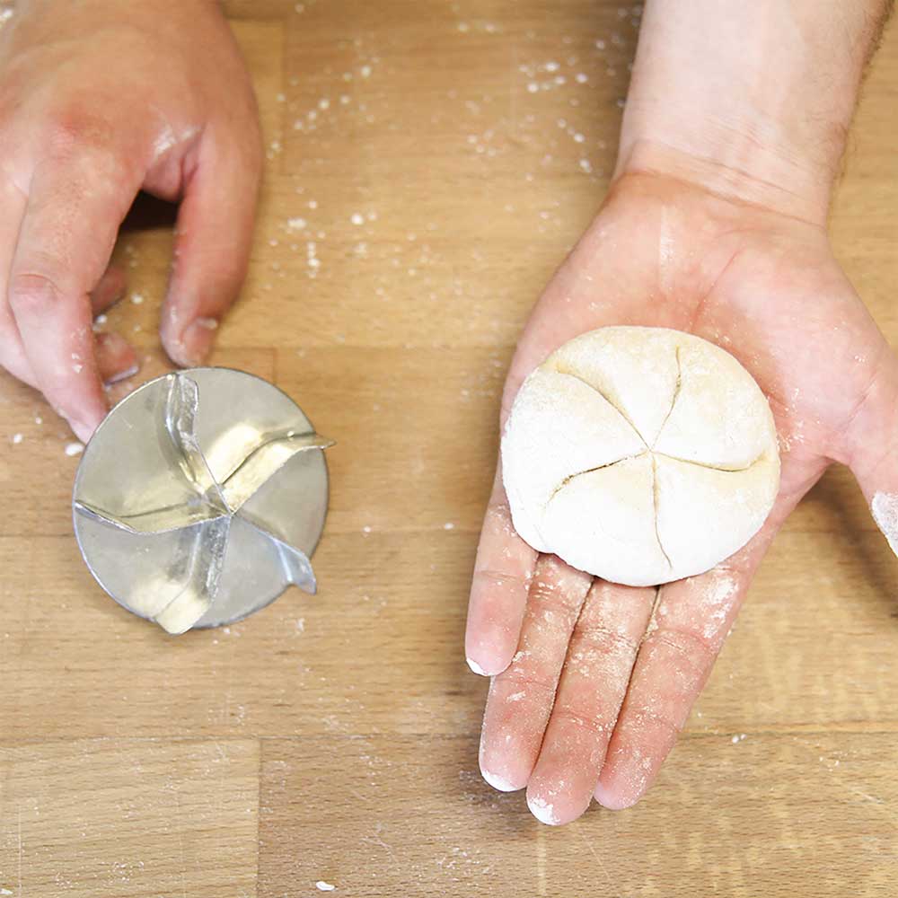 Zu sehen sind zwei Hände. Die eine Hand hält den Brötchendrücker und in der anderen Hand liegt das Brötchen elches noch nicht ausgebacken ist.