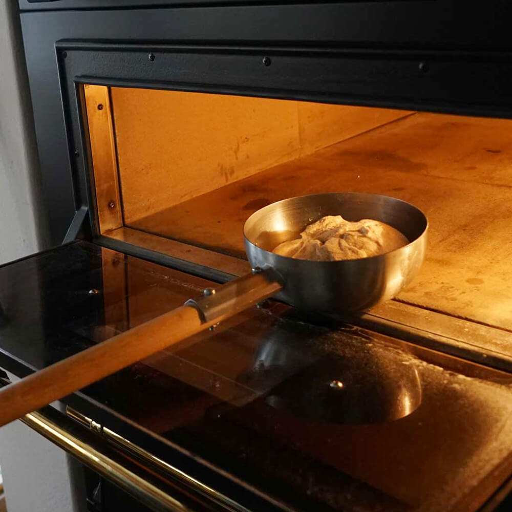 In einen geöffneten Ofen wird gerade ein Teigling mit einer Einnetzschüssel gelegt.