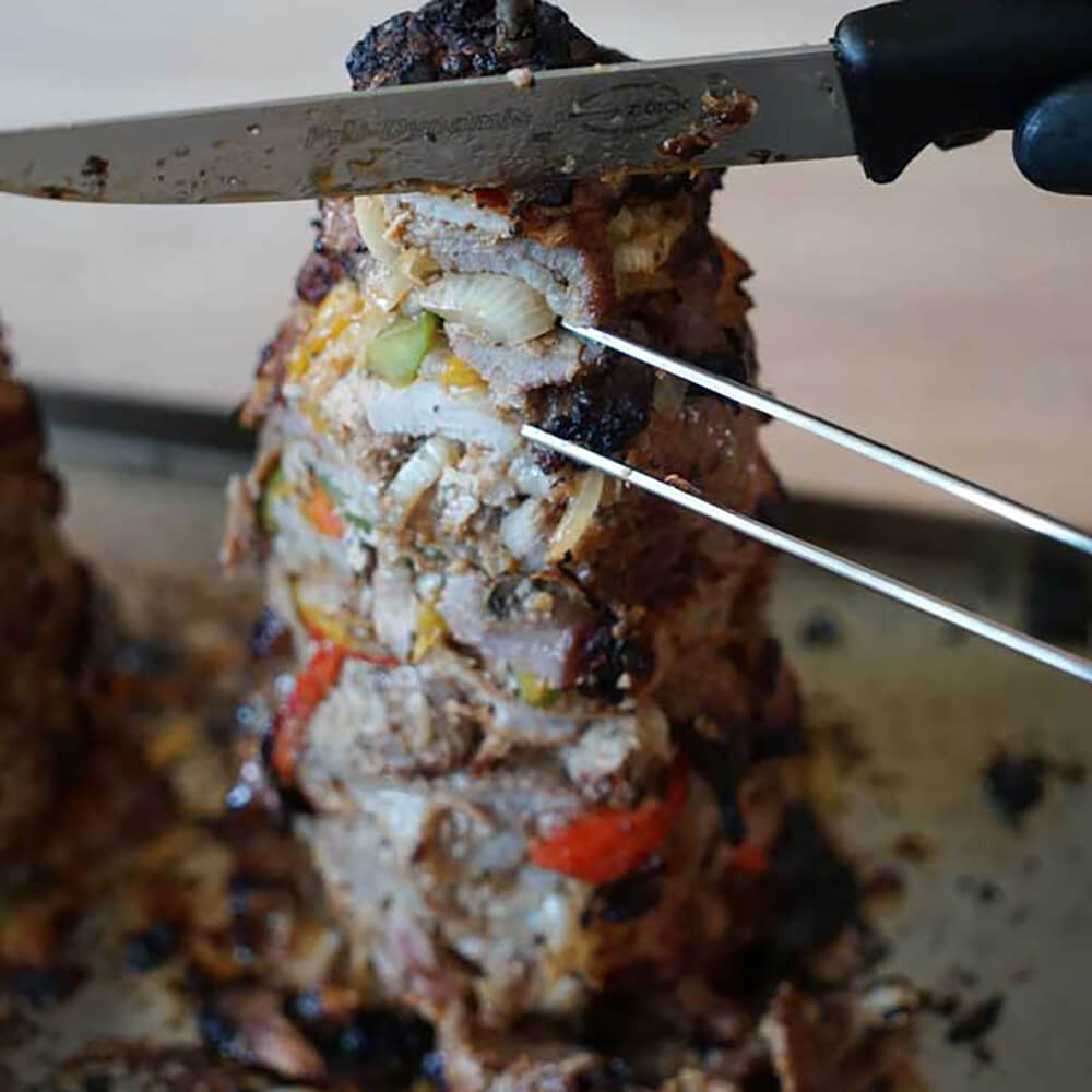 Ein fertig gebratener Gyrosspieß wird seitlich mit einem Messer aufgeschnitten