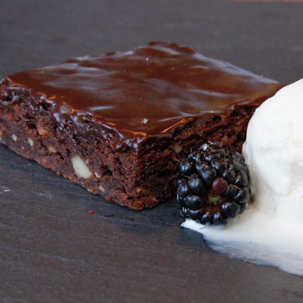 Schoko Brownie mit Nüssen und einer Schokoladen Ganache mit einer Brombeere und Vanilleeis auf einem Schieferteller angerichtet