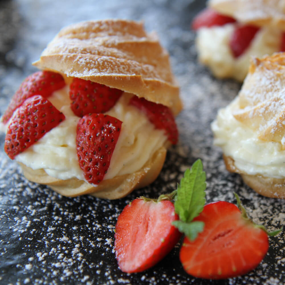 Rezept für Windbeutel WInbeutel mit Puderzucker bestreut und einer Füllung aus Sahne und Erdbeeren auf einer Schieferplatte serviert