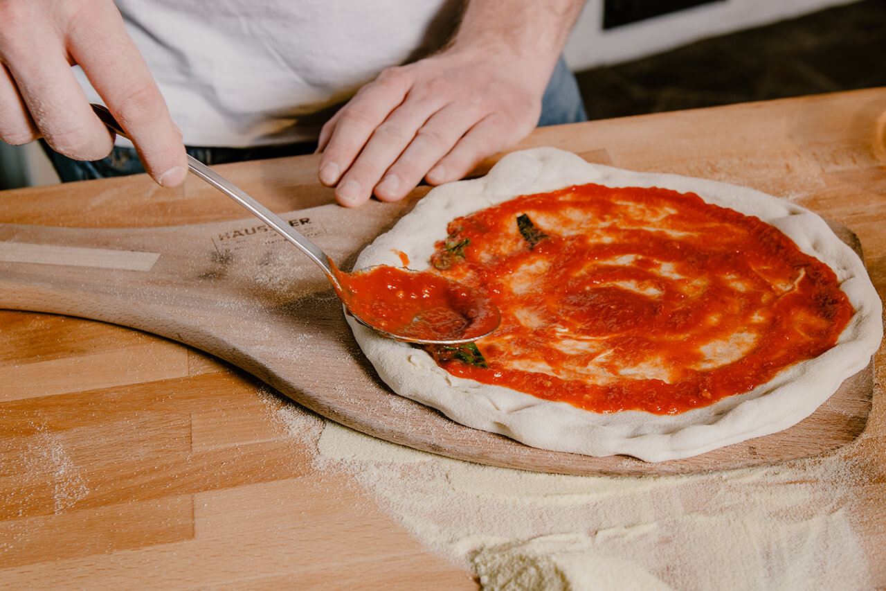 Pizza Pizza wird mit Tomatensoße bestrichen