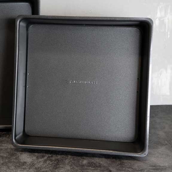 Kuchenform mit Hebeboden Kuchenform schwarz und quadratisch aufrecht vor einer Wand aufgestellt.