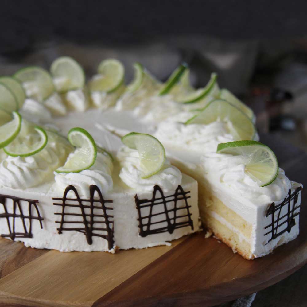 Ein Kuchen mit Sahneröschen und Scheiben von Limetten steht aufgeschnitten auf einer Kuchenplatte.