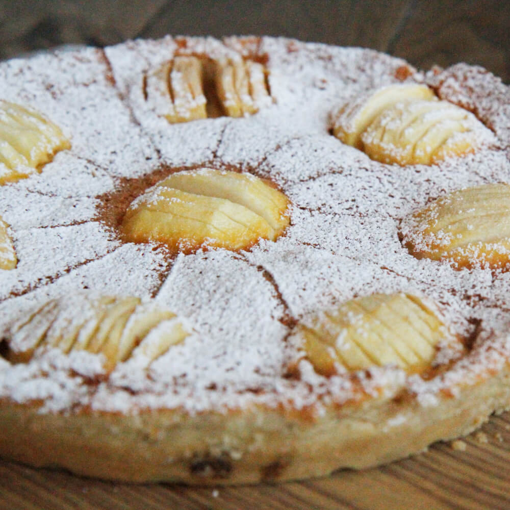 Rezept für Frucht-Tarte leckere Frucht-Tarte mit Äpfeln oben drauf und mit Puderzucker bestreut, auf einem Backbrett serviert