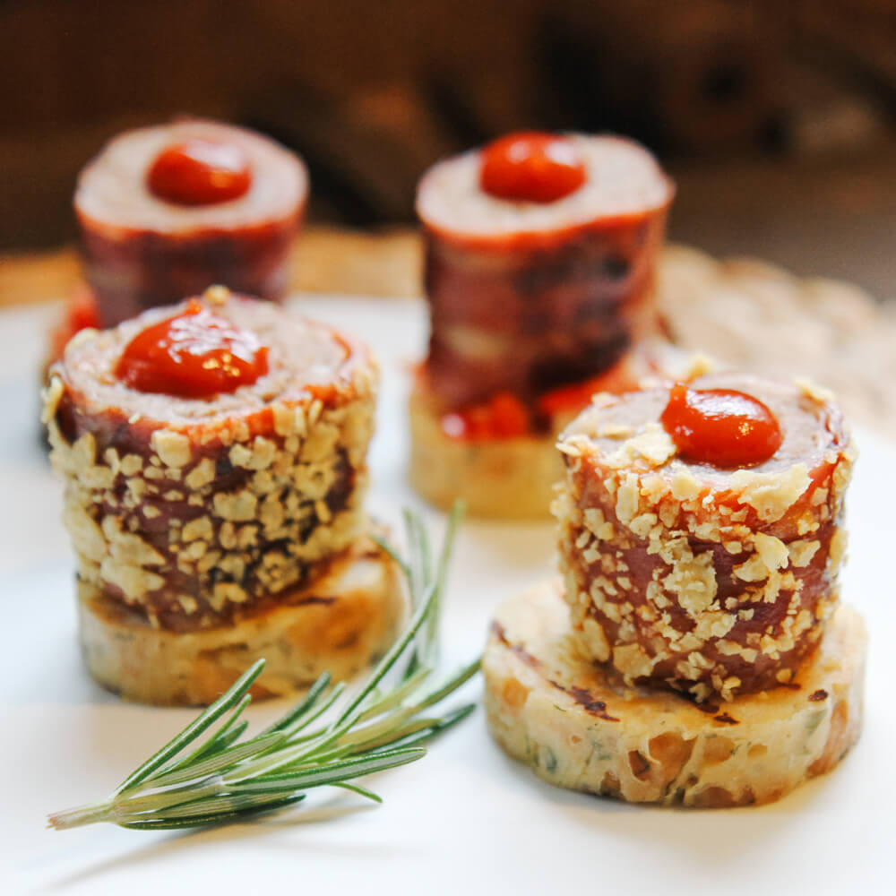 Hackfleischrolle mit einem Mantel aus zerbröselten Tortilla Chips, auf einem Semelknödeltaler serviert und mit Salsa oben drauf garniert. 