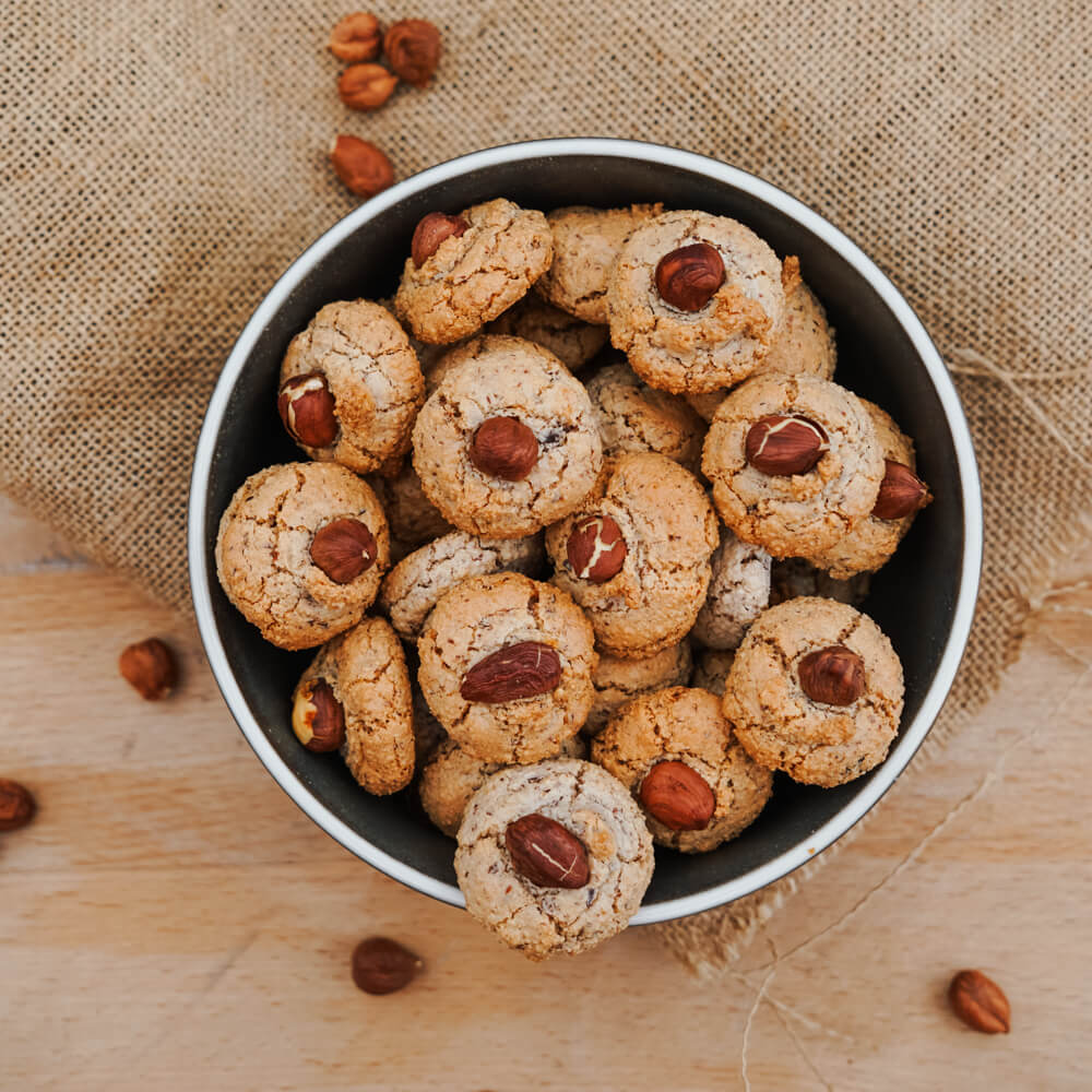 Rezept für Nussmakronen Nussmakronen mit einer Haselnuss verziert in einer dunkelblauen Schüssel