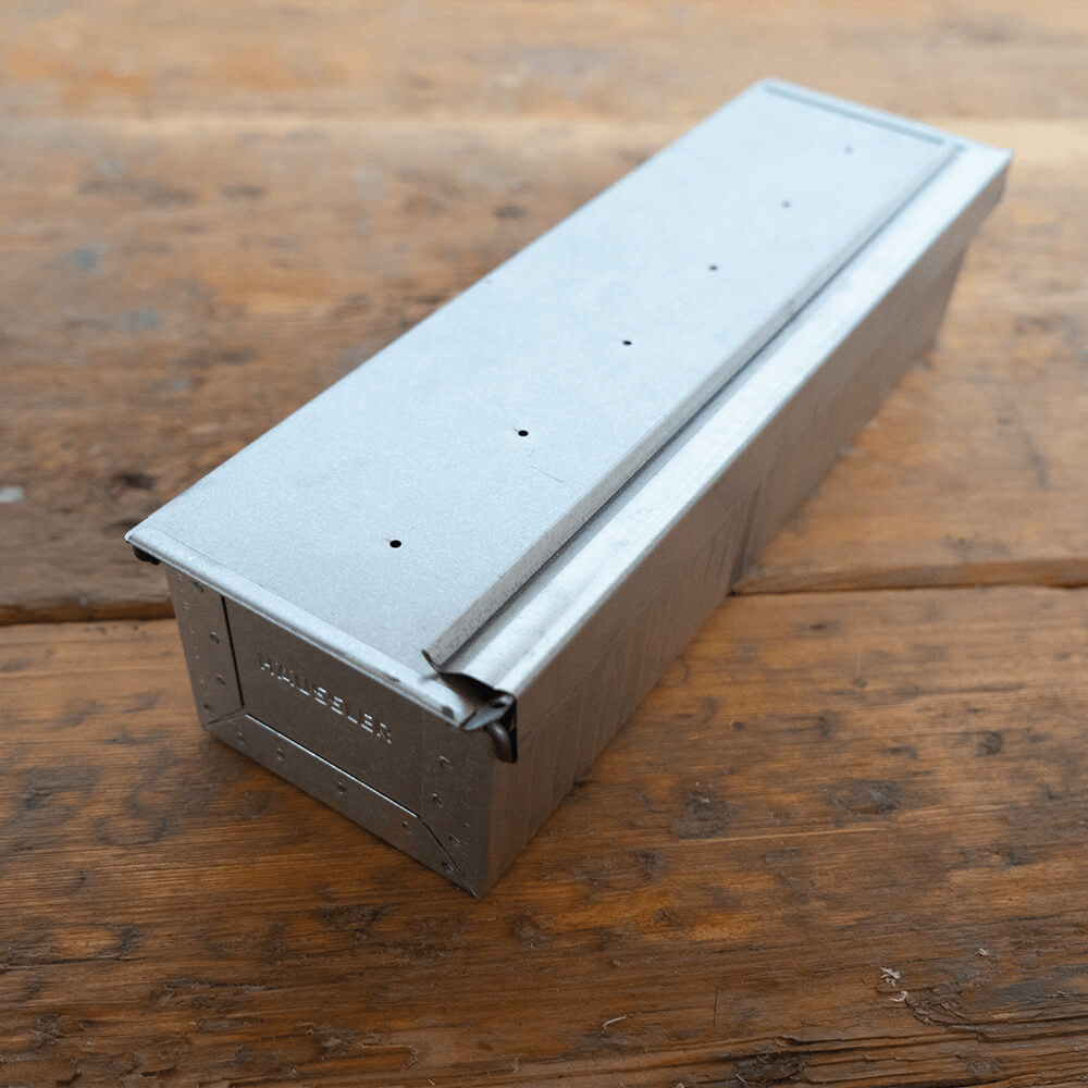 Mittlere Toastbrotform Mittlere Toastbrotform in seitlicher Ansicht aus aluminiertem Stahl auf einem Holz-Untergrund. Der Deckel ist geschlossen.