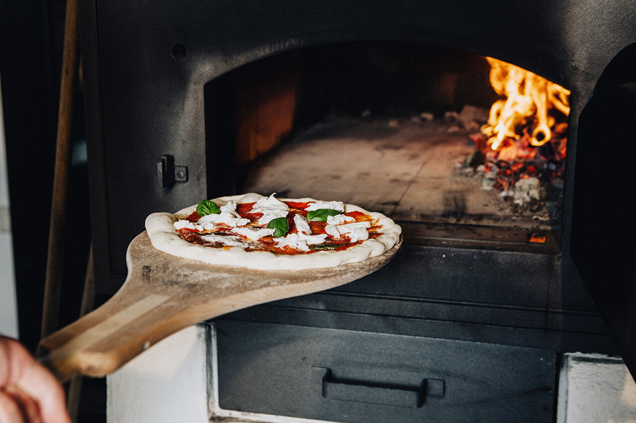 Pizzaofen Pizza wird in Holzbackofen eingeschossen