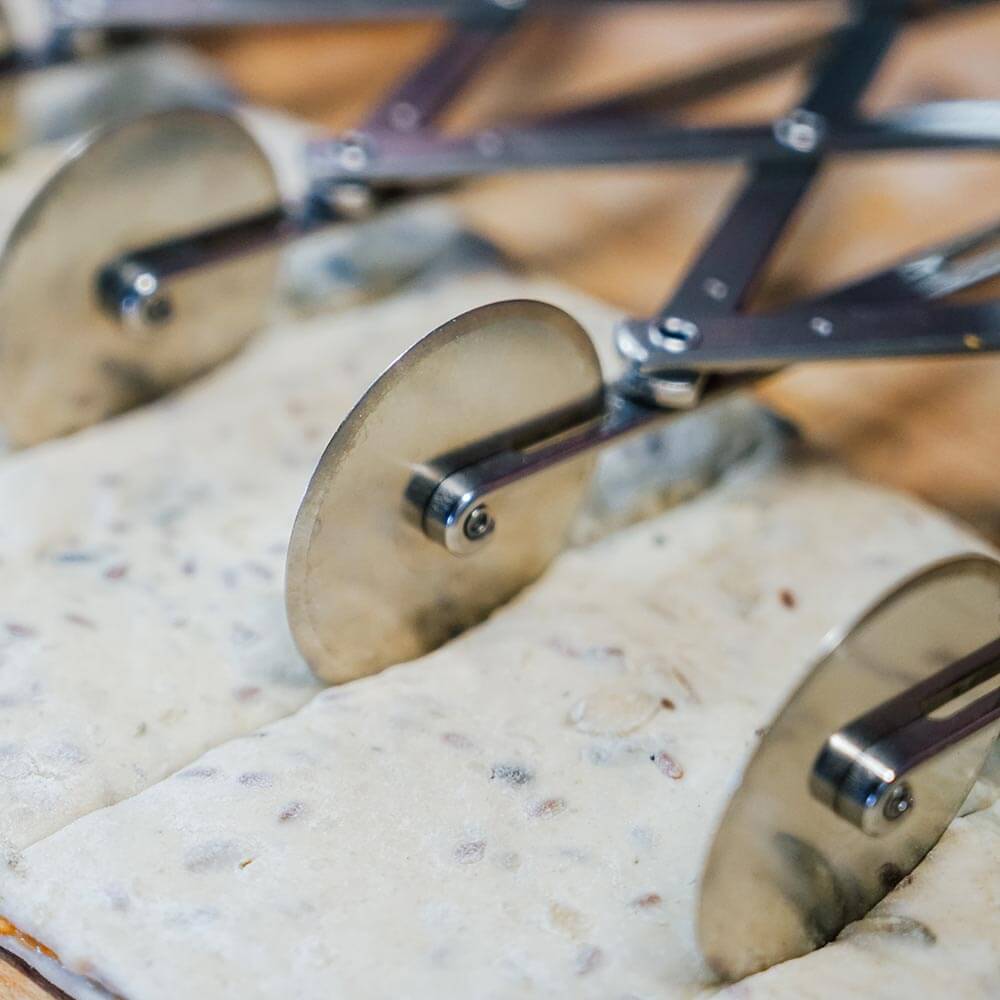 Teigschneider Es wird im Nahen gezeigt wie der Teigschneider die dünne Teigfläche auf dem Tisch gleichmäßig schneidet.