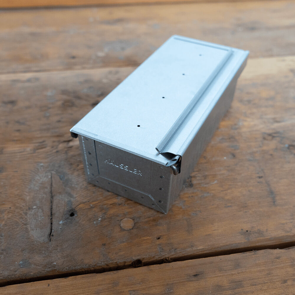 Kleine Toastbrotform Kleine Toastbrotform in seitlicher Ansicht aus aluminiertem Stahl auf einem Holz-Untergrund. Der Deckel ist geschlossen.